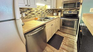 A compact kitchen with white cabinets, a microwave, an oven, a dishwasher, and a tiled backsplash. - Relaxing 1Br Condo sleeps 4.  Pool outside back door.  Beach Access.   (Panama City Beach)