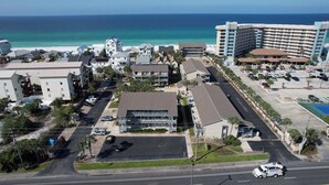 An aerial view of a coastal hotel area with multiple buildings, a parking lot, and a view of the ocean. - Relaxing 1Br Condo sleeps 4.  Pool outside back door.  Beach Access.   (Panama City Beach)