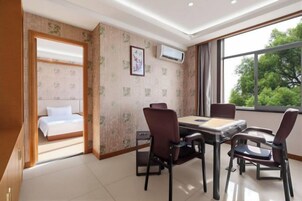 Una habitación de hotel con cama, una mesa de comedor con sillas, una ventana con vista a árboles y un equipo de aire acondicionado en la pared.
