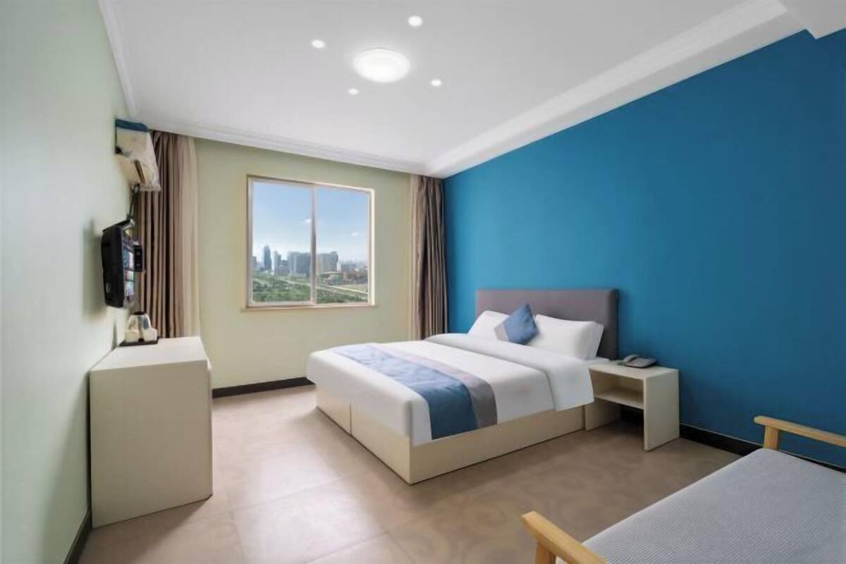 A hotel room with a large bed, a bedside table, a nightstand, a desk, and a window with a city view.