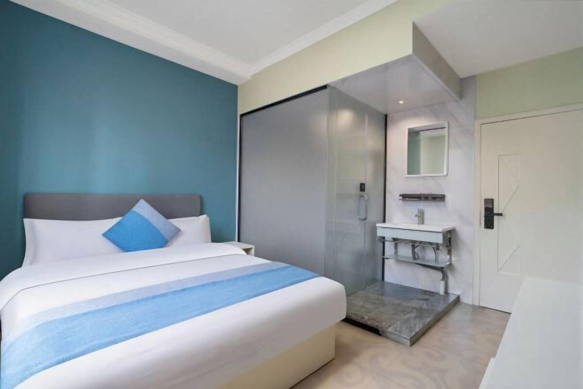 A modern hotel room with a large bed, a shower area, and a small bathroom.