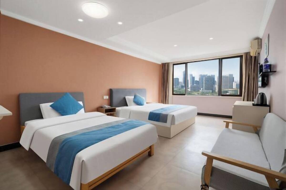 A hotel room with two beds, a sofa, a desk, and a large window with a city view.