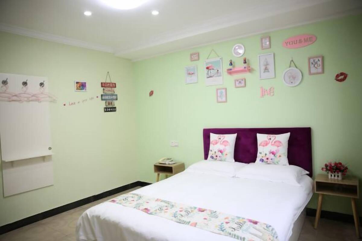 Quarto com cama, mesa de cabeceira, parede com quadros e decorações, e um quadro branco.