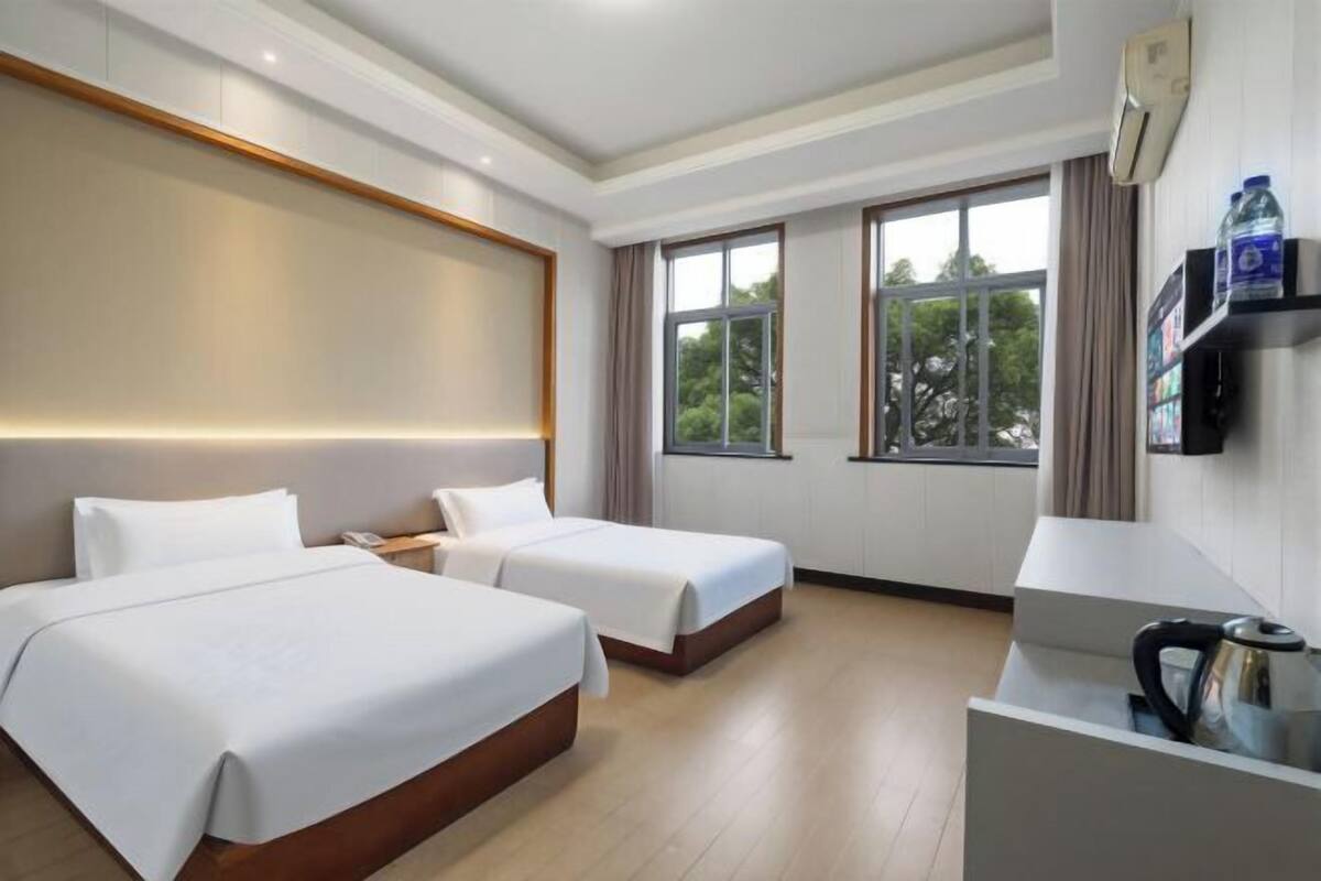 A hotel room with two beds, a bedside table with a phone, a coffee maker, and a window with a view of trees.