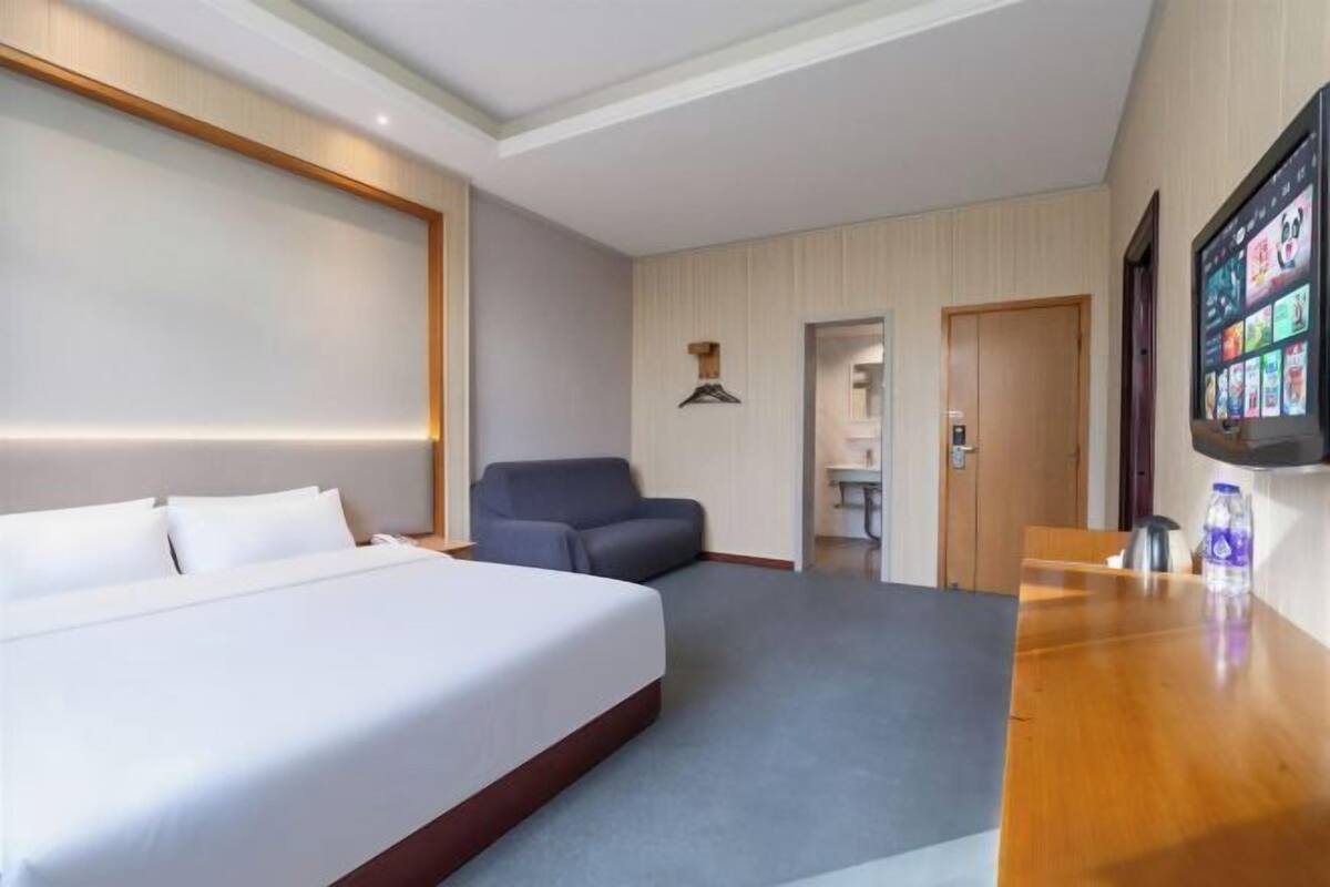 A hotel room with a bed, a desk, a chair, a TV, and a door.