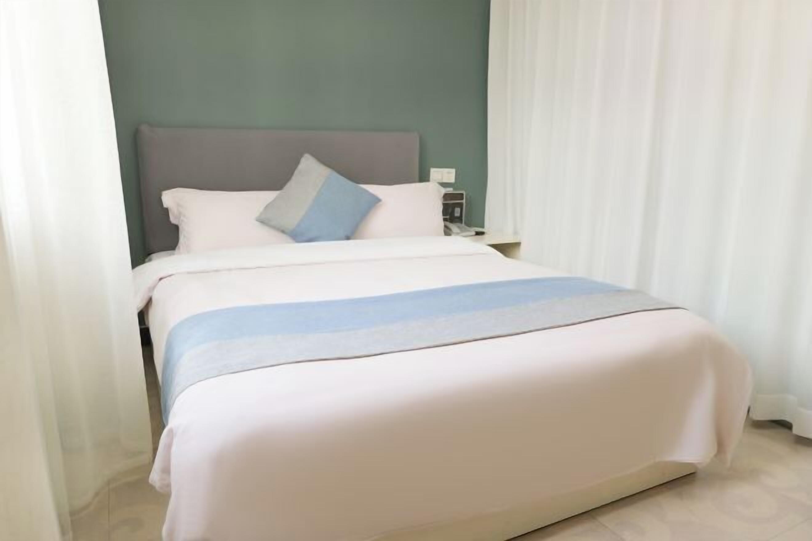 A neatly made bed with a grey headboard, white and blue pillows, and a white and blue striped blanket.