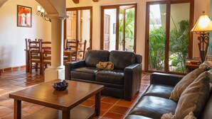 A spacious living area with a leather sofa, a wooden coffee table, and a dining area with wooden chairs and a table.