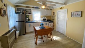 A compact kitchen with white cabinets, a stainless steel refrigerator, a microwave, and a ceiling fan. - Cape Escape Cottage (Yamouth)