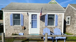 A small house with a front porch, two blue Adirondack chairs, and an American flag. - Cape Escape Cottage (Yamouth)