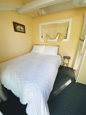 A bedroom with a bed, a window with curtains, a small table, and a wall-mounted picture.