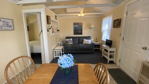 A cozy living room with a wooden dining table, a grey sofa, and a TV on a white stand. - Cape Escape Cottage (Yamouth)