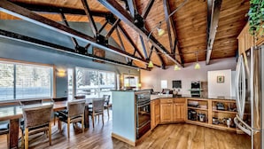 A modern kitchen with wooden beams, a large island, and a stainless steel refrigerator.