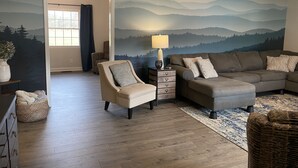 A living room with a mountain mural, a sofa, a chair, a lamp, and a wooden floor.