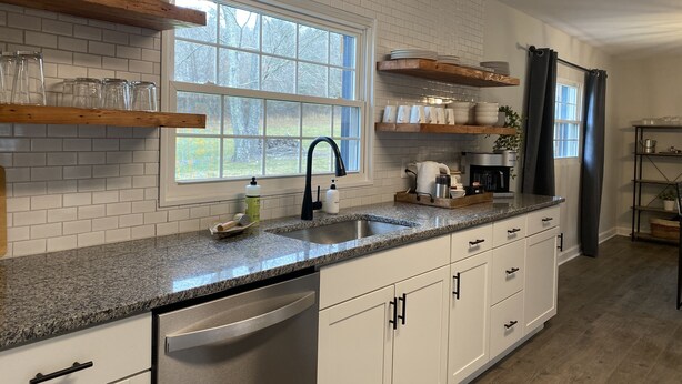 A kitchen with white subway tiles, granite countertops, a dishwasher, and wooden shelves.