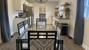 A modern kitchen with white cabinets, a central island, and a dining area with a glass table and patterned chairs.