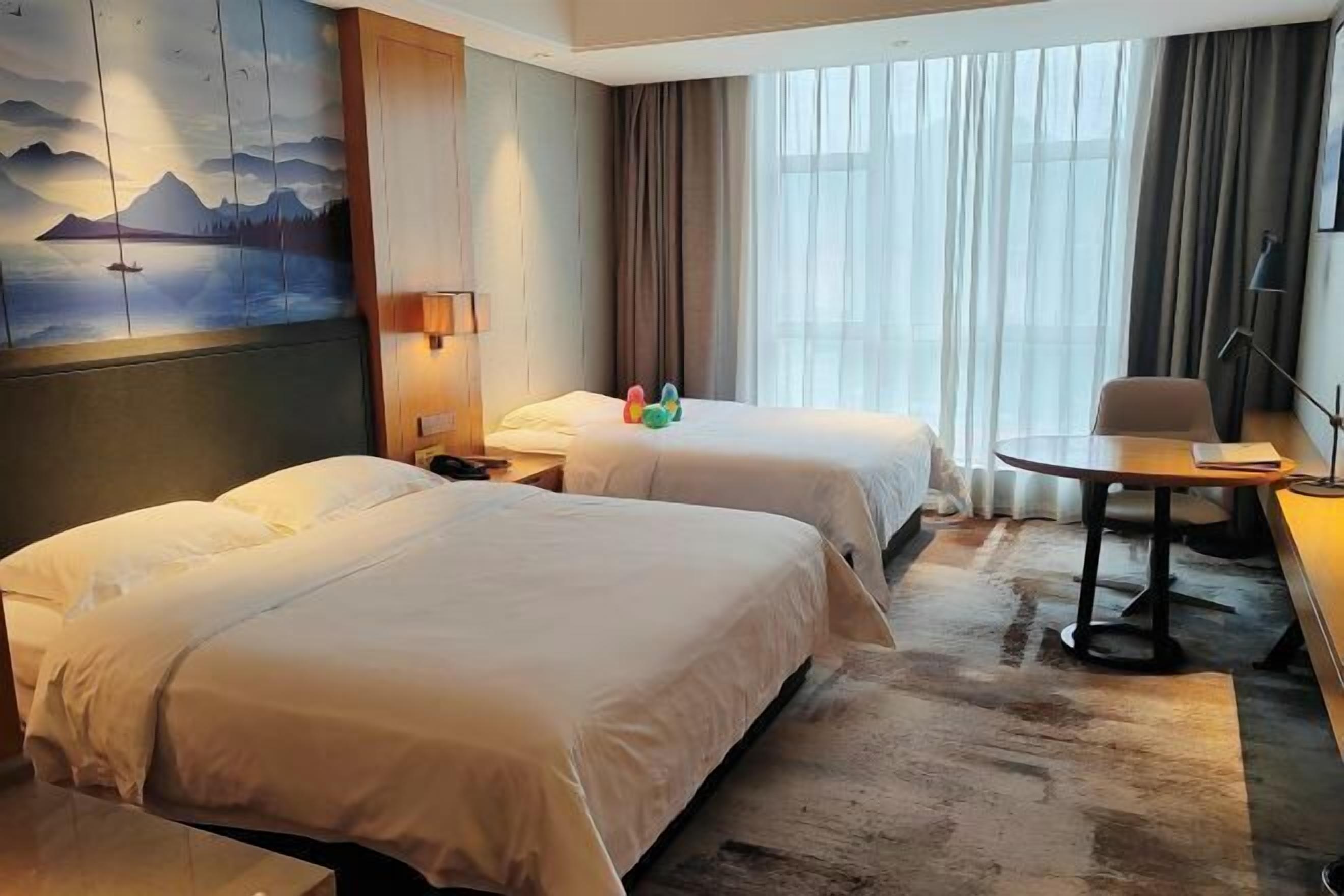A hotel room with two beds, a desk, a chair, a lamp, and a painting on the wall.