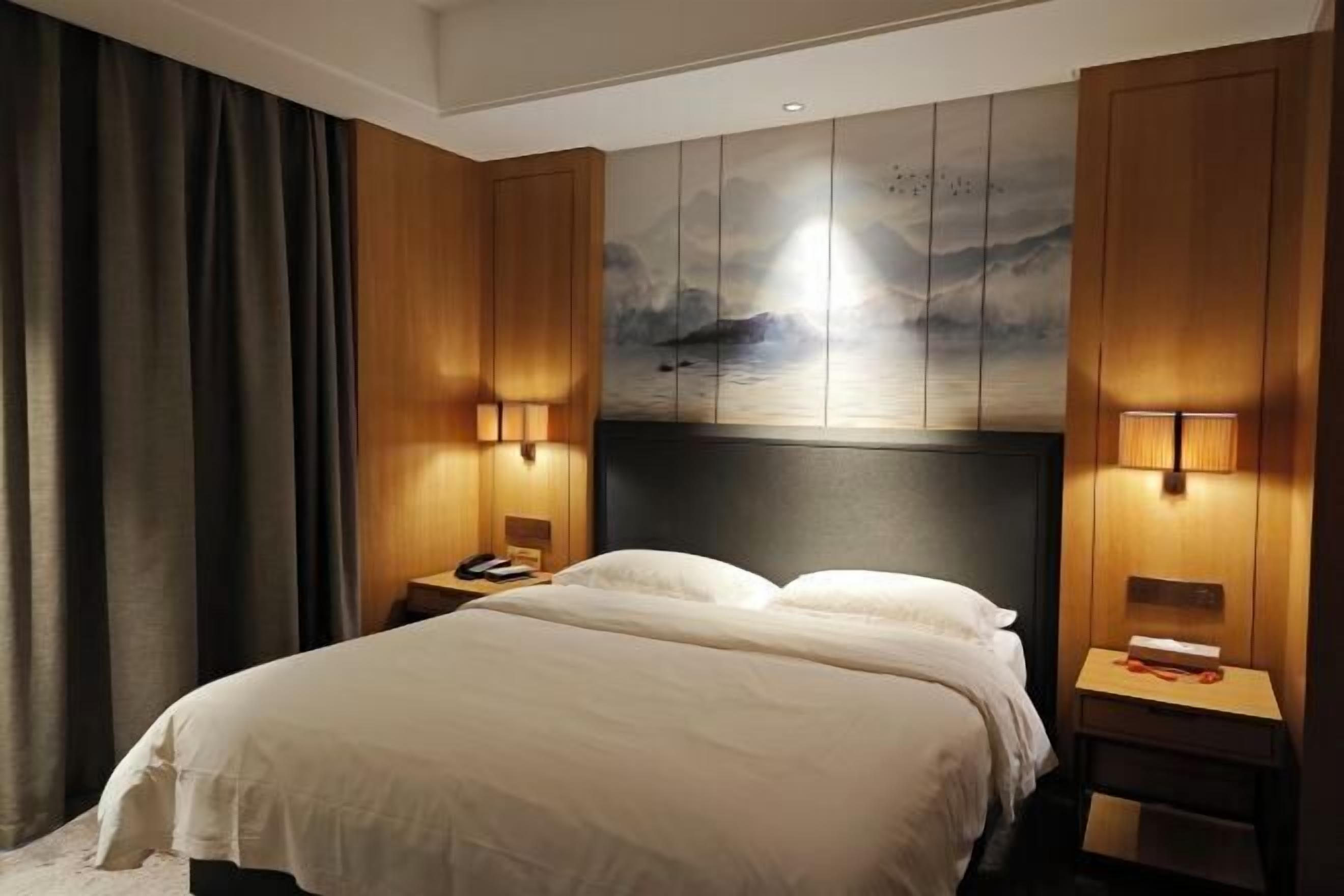 A hotel room with a large bed, wooden paneling, a painting on the wall, and two bedside lamps.