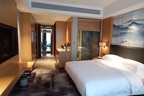 Une chambre d’hôtel avec un grand lit, une télévision, une salle de bain avec un miroir et un tableau au mur.
