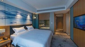 A hotel room with a bed, a nightstand, a wall-mounted TV, and a bathroom visible through a glass door. - Zhanpeng International Hotel (Chongzuo)