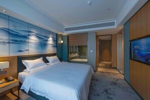 Une chambre d’hôtel comprenant un lit, une table de chevet, un téléviseur fixé au mur et une salle de bain visible à travers une porte en verre.