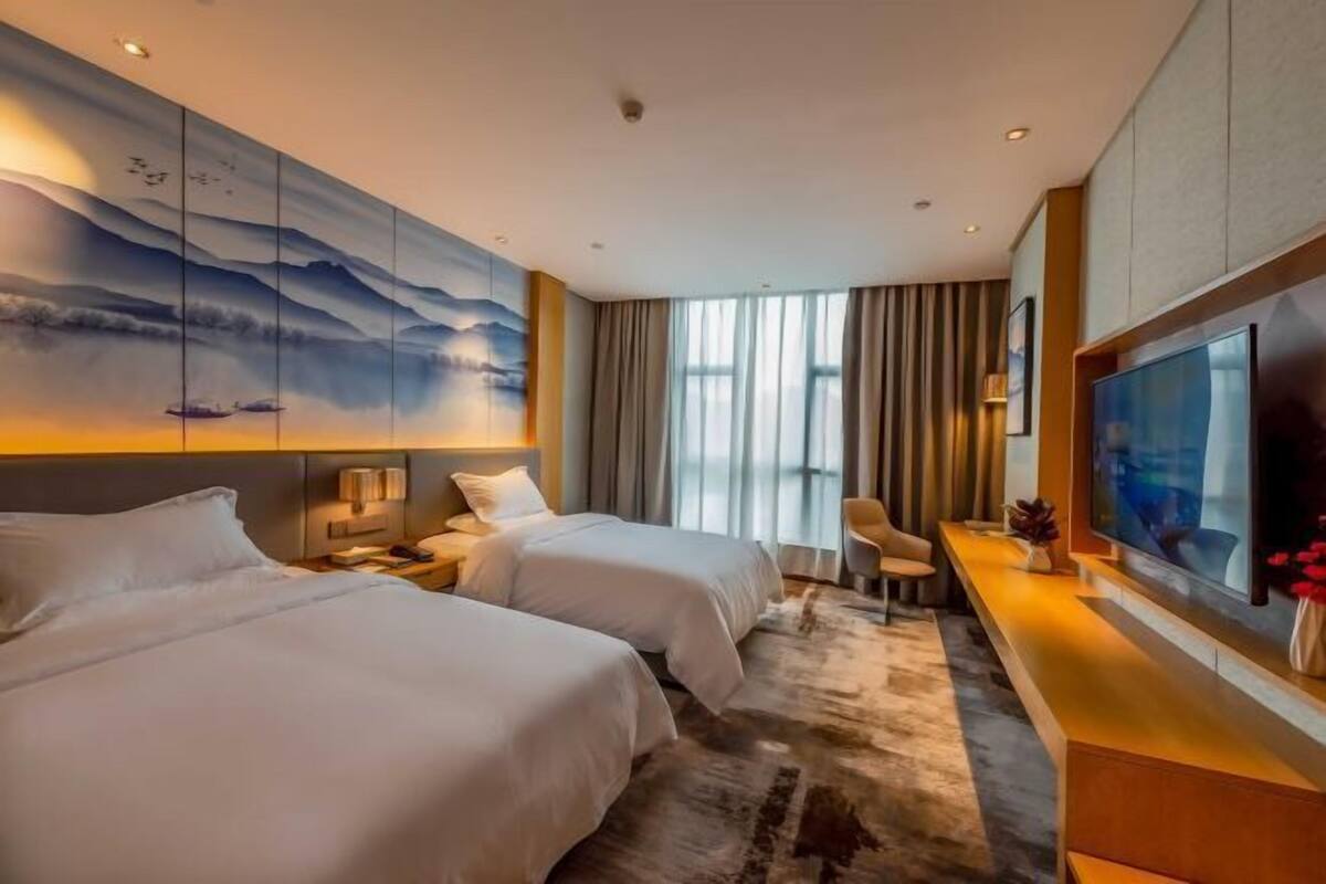Una habitación de hotel con dos camas, un televisor grande, un escritorio y un cuadro en la pared.