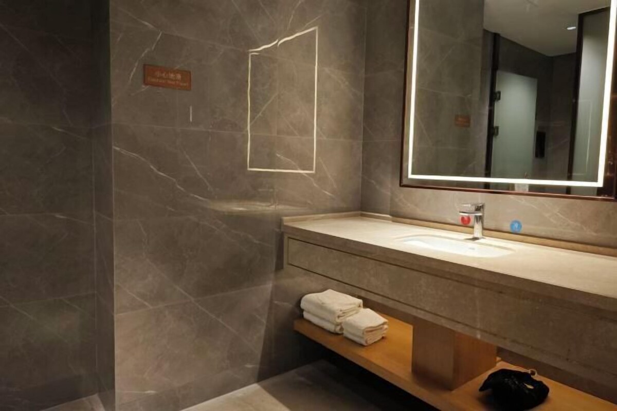 Une salle de bain moderne avec un mur en marbre, un grand miroir, un lavabo et un porte-serviettes.