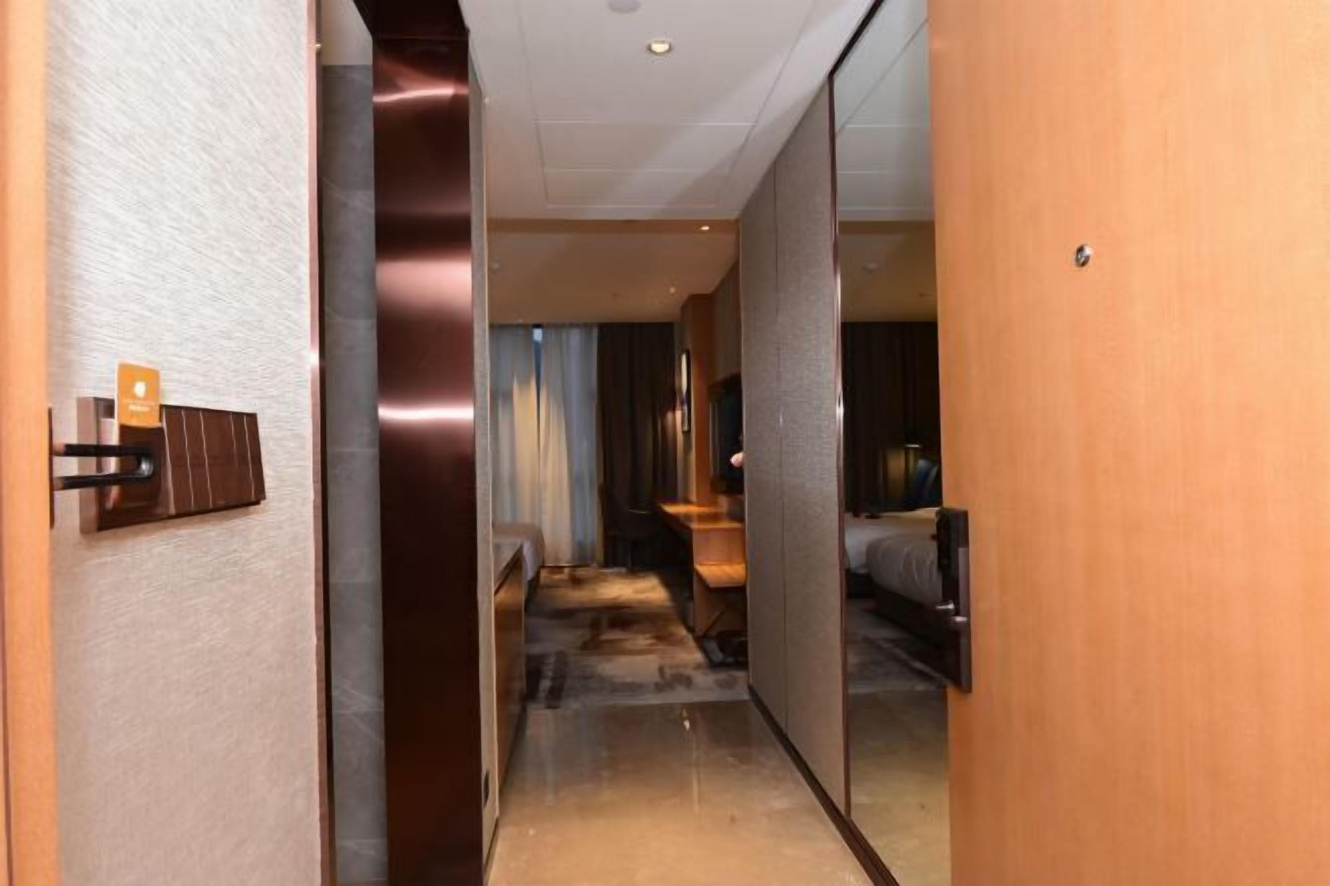 A hotel corridor with a wooden door, a reception desk, and a bed in the distance.