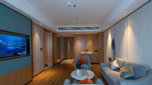 A modern hotel room with a flat-screen TV, a sofa, a chair, a small table, and a kitchen area. - Zhanpeng International Hotel (Chongzuo)