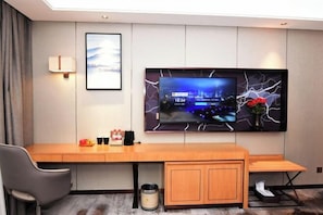 Ein Hotelzimmer mit einem Holztisch, einem an der Wand befestigten Fernseher, einem gerahmten Bild und einem kleinen Mülleimer.