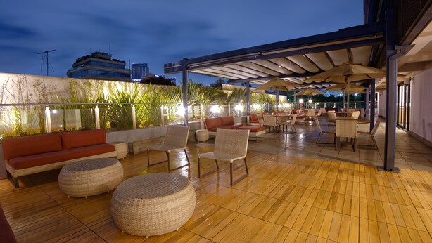 An outdoor patio with wicker furniture, a red sofa, and a covered seating area with umbrellas. - Golden Tower Express Berrini by Fenix Hoteis (São Paulo)