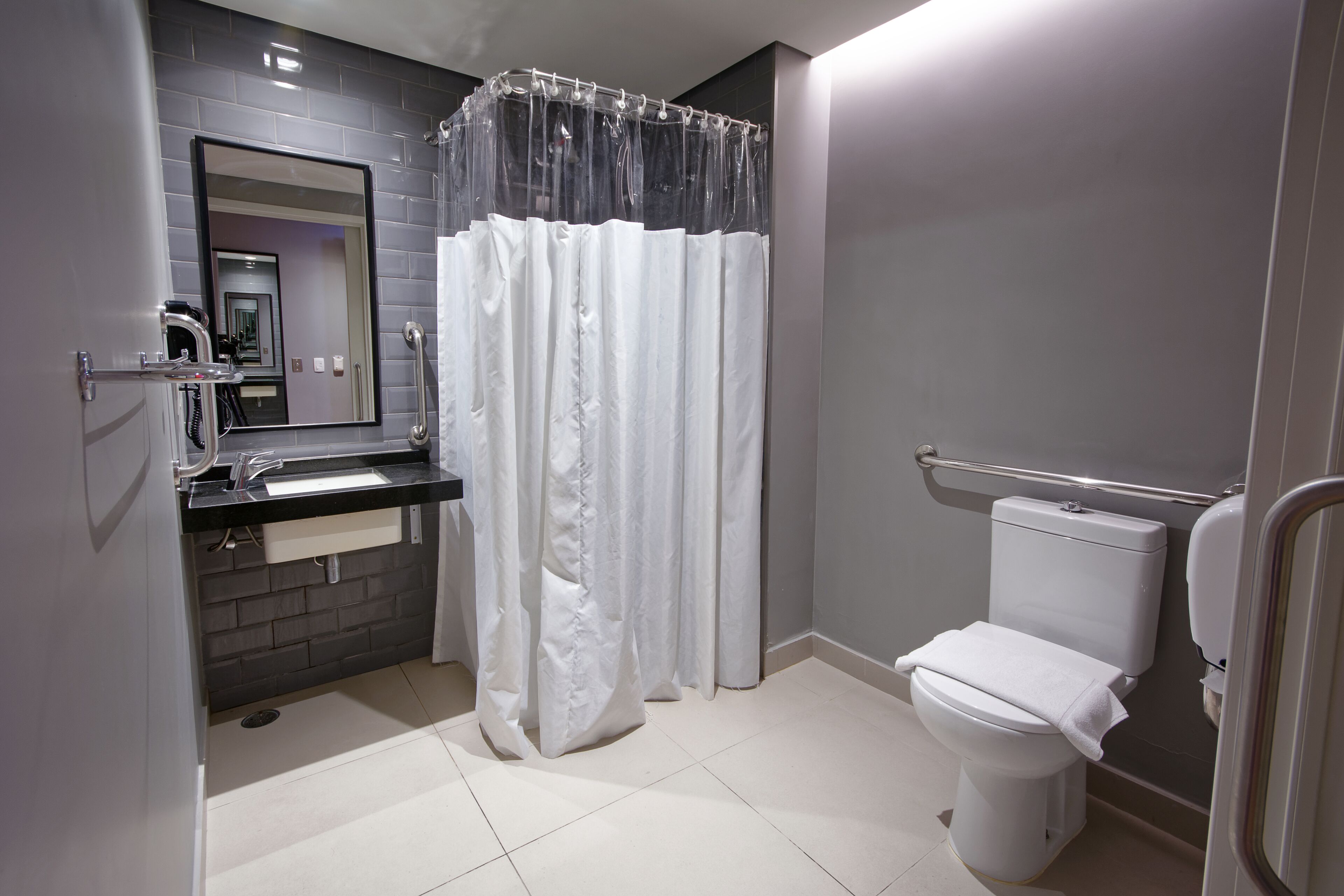 A modern bathroom with a white toilet, a sink with a mirror above it, and a shower curtain.
