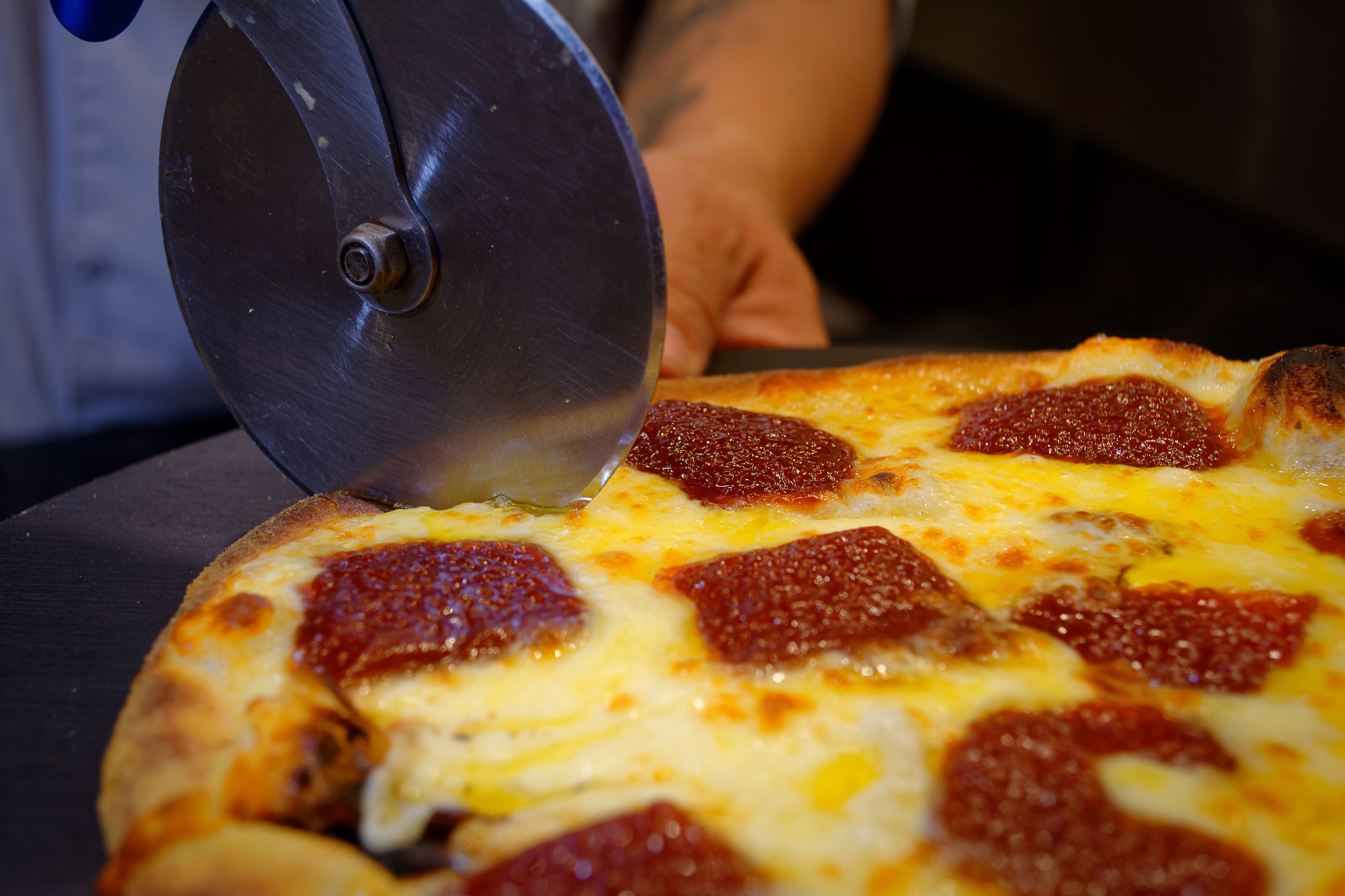 A pizza being sliced with a metal pizza cutter.