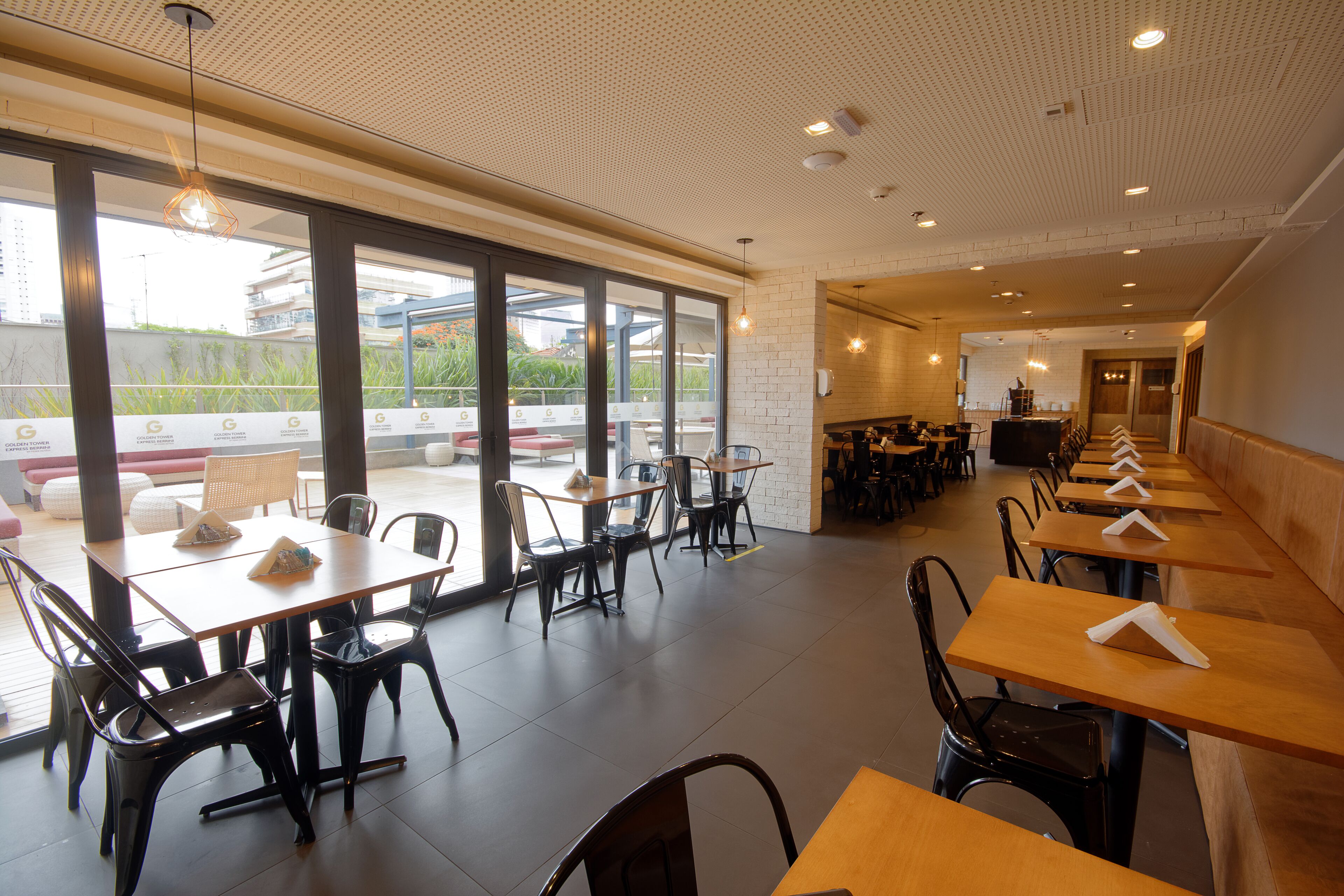 Un restaurante espacioso con mesas y sillas altas, ventanas amplias y un diseño de techo moderno.