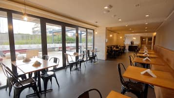 Un restaurante espacioso con mesas y sillas altas, ventanas amplias y un diseño de techo moderno.
