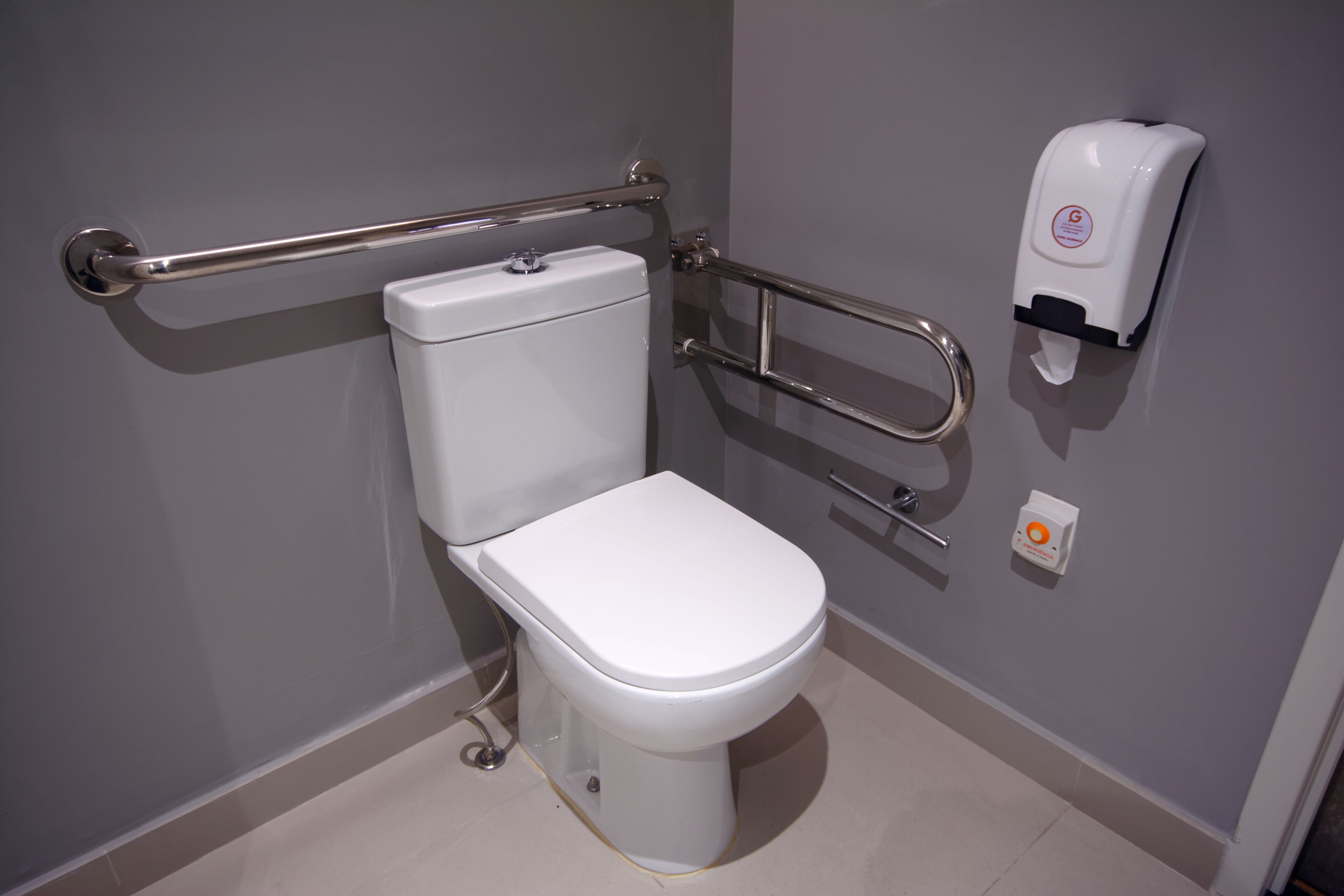Een moderne badkamer met een wit toilet, handgrepen en een zeepdispenser.