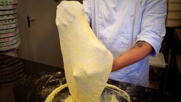A person in a blue shirt handling a large piece of dough on a black countertop.