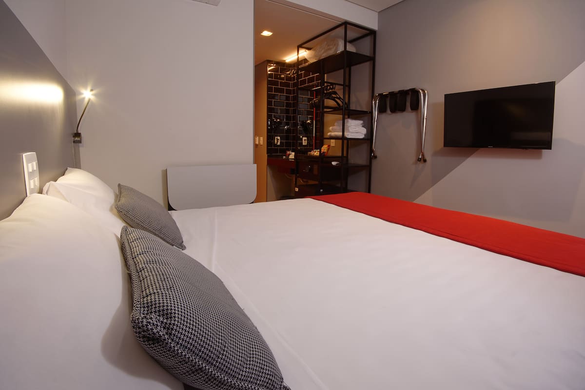 Ein Hotelzimmer mit einem Bett, einer roten Bank, einem an der Wand befestigten Fernseher und einem Schrank mit Regalen.