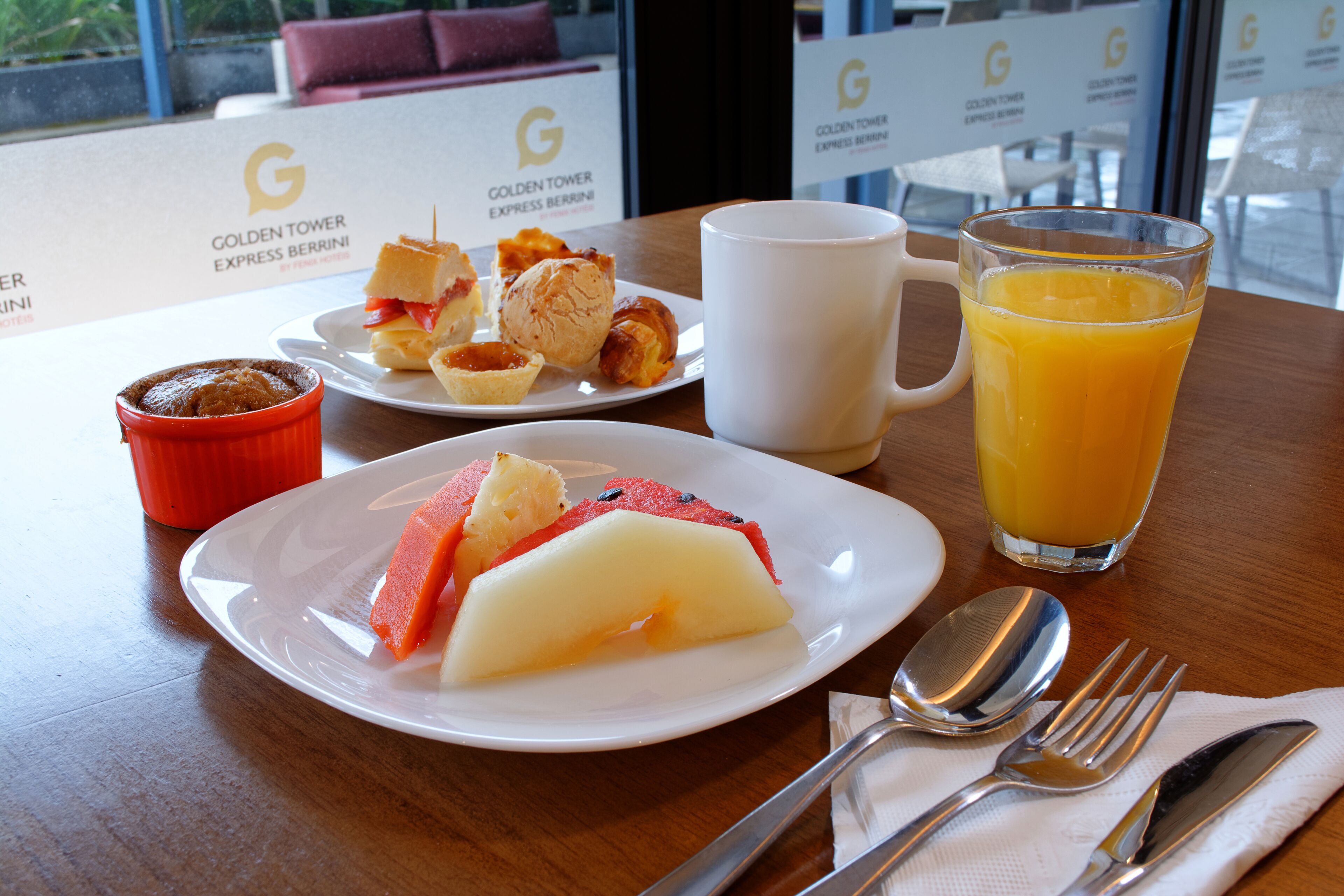 Colazione servita con un piatto di frutta, un bicchiere di succo d'arancia e un muffin su un tavolo.