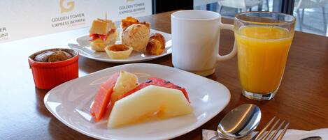 Colazione servita con un piatto di frutta, un bicchiere di succo d'arancia e un muffin su un tavolo.