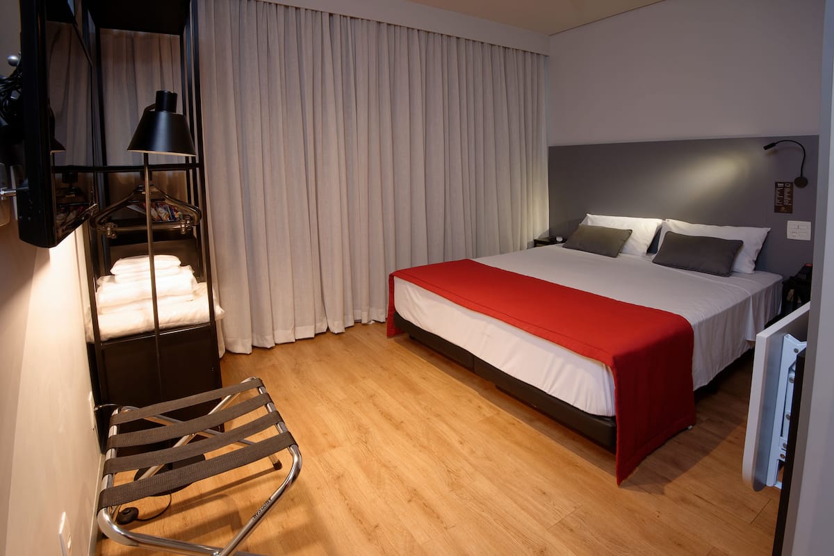 Ein Hotelzimmer mit einem Bett, einer roten Decke, einem Hängestuhl und einem Regal mit Handtüchern.