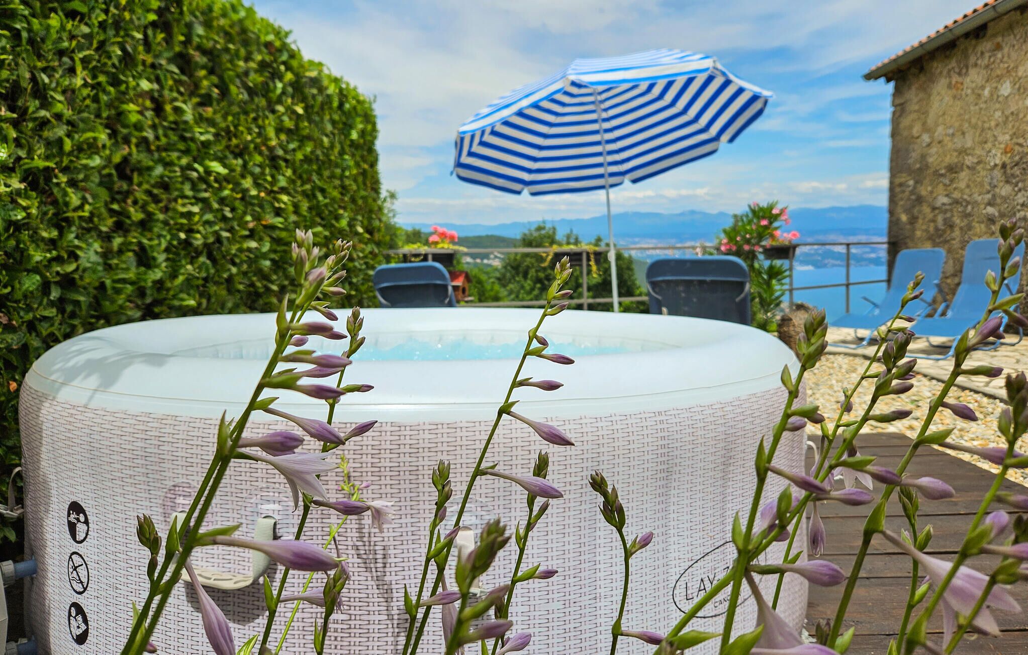 Uma banheira de hidromassagem cercada por vegetação, uma piscina e vista para o mar.