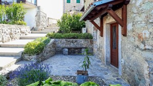 A stone courtyard with steps leading to a wooden door, surrounded by lush greenery and a small garden with lavender. - Beautiful home in Lovran with WiFi (Lovran)
