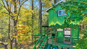Une cabane en bois peinte en vert, avec un toboggan, entourée d’arbres.