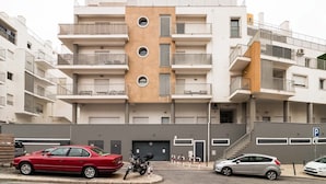 Un immeuble résidentiel à plusieurs étages, doté de balcons, d’un espace de stationnement et d’une moto garée devant.