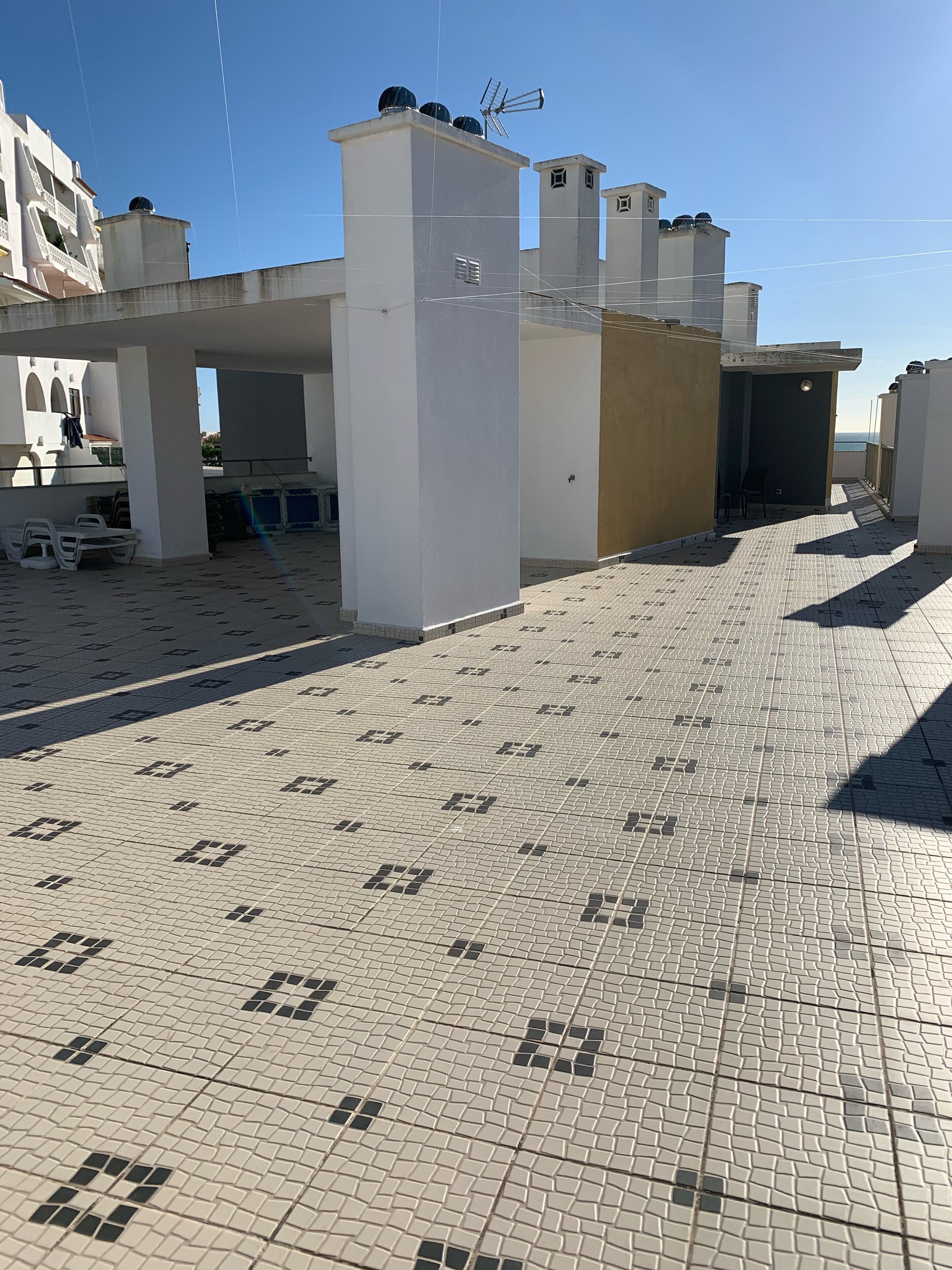 A rooftop terrace with tiled flooring, white pillars, and a view of the sea.