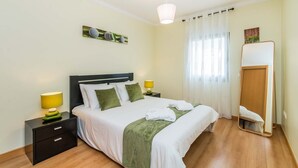 Une chambre bien rangée, avec un lit, des tables de chevet, un miroir et une fenêtre avec des rideaux.