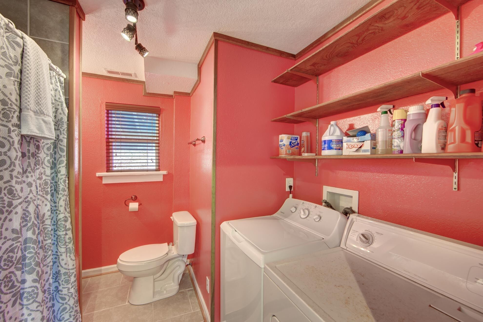 A bathroom with a toilet, a washing machine, and shelves with cleaning supplies.
