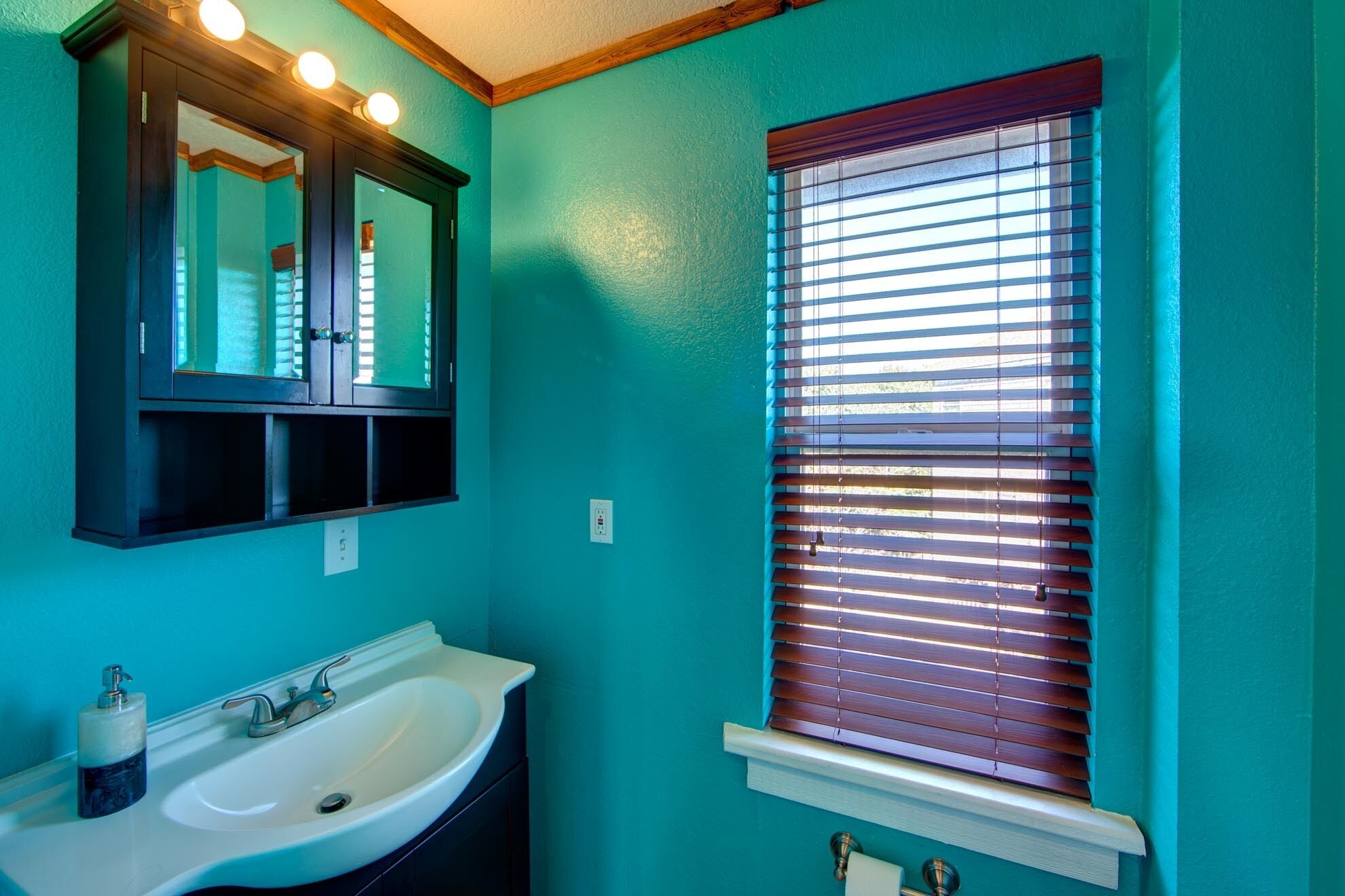 Une salle de bain avec un lavabo, un miroir et une fenêtre équipée de stores.
