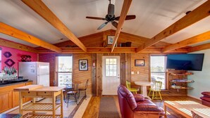 A cozy cabin interior with a wooden ceiling, a dining area, a living room with a leather sofa, and a kitchen with a refrigerator and a sink. - Surf Chalet w/ hot tub and kayaks (Avon)