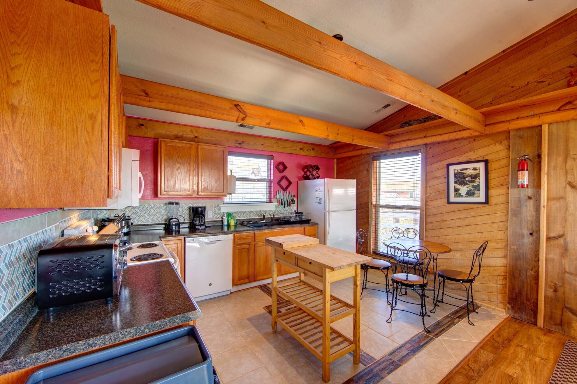A cozy kitchen with wooden cabinets, a granite countertop, a sink, a stove, and a refrigerator. There is a dining table with chairs and a window with blinds.